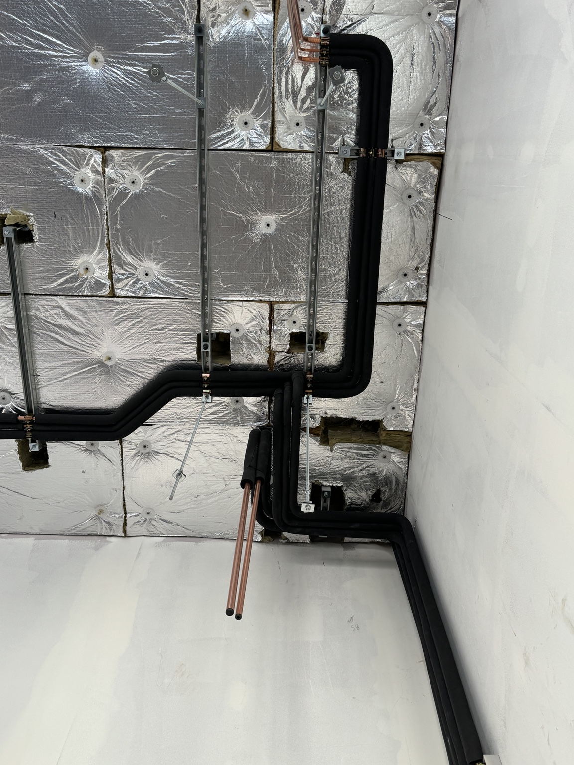 Neatly supported insulated VRF refrigeration pipework changing level through a ceiling void